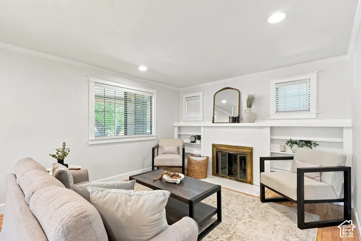 Recessed lighting, crown molding, white fireplace with brass-finish doors, built-in shelving, and wood-finish flooring