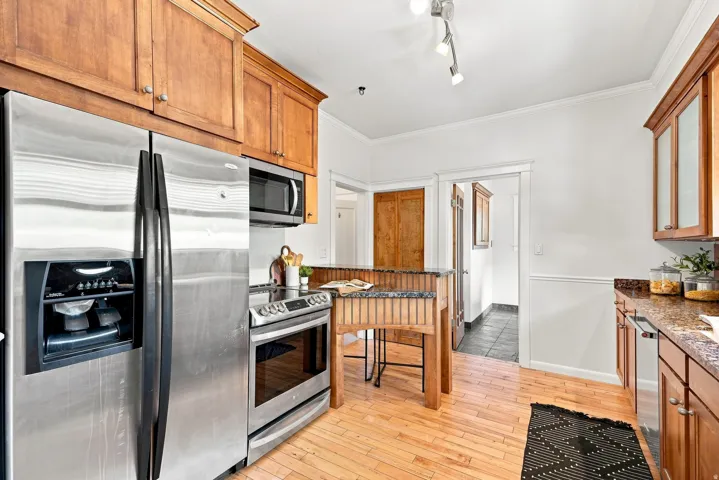 Warm wood cabinetry and warm wood-finish flooring define this kitchen, which features stainless steel appliances including a side-by-side refrigerator, gas range, and built-in microwave
