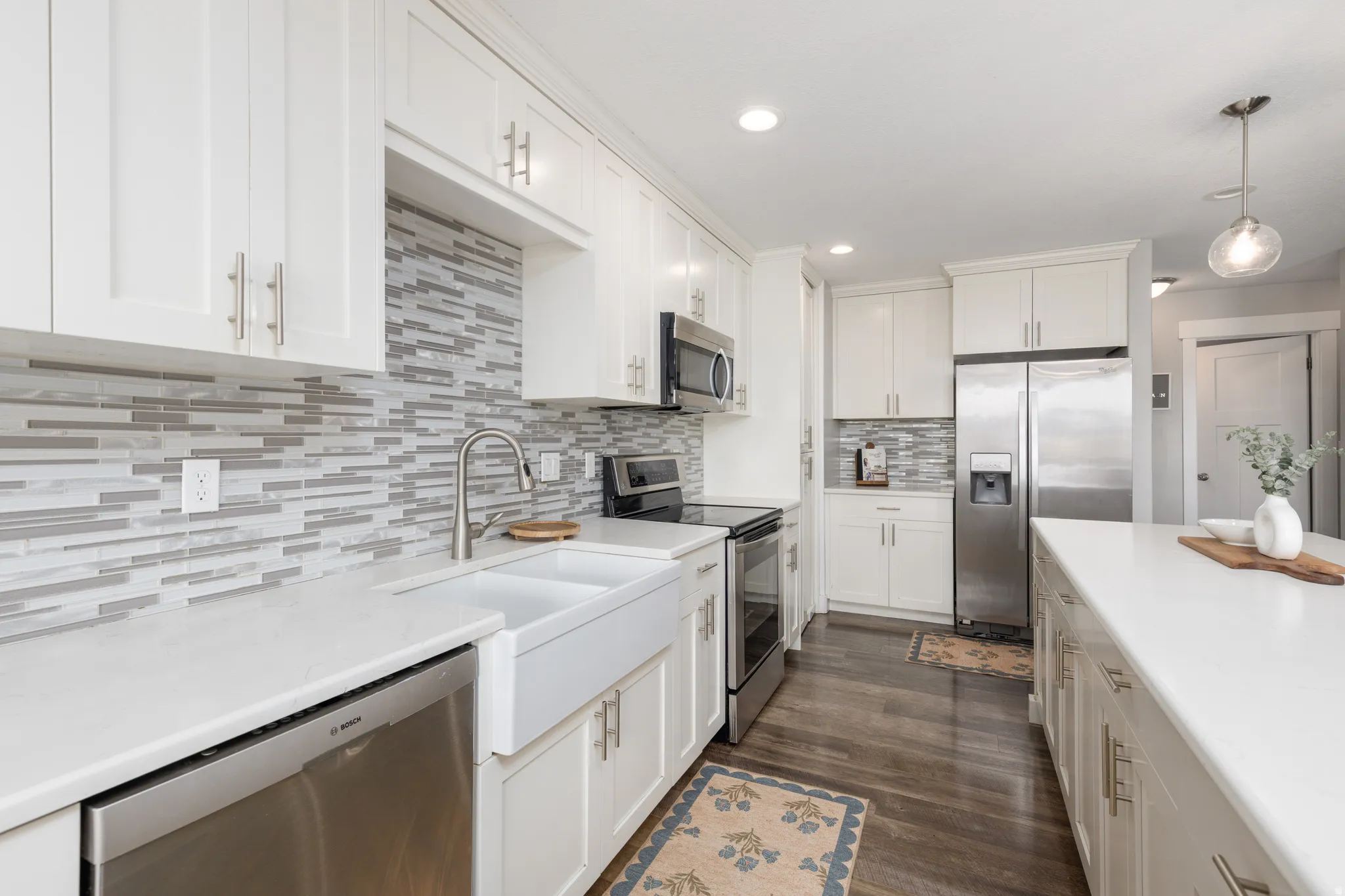 White shaker cabinetry, light-toned countertops, tile backsplash, stainless steel appliances, and dark wood-finish flooring