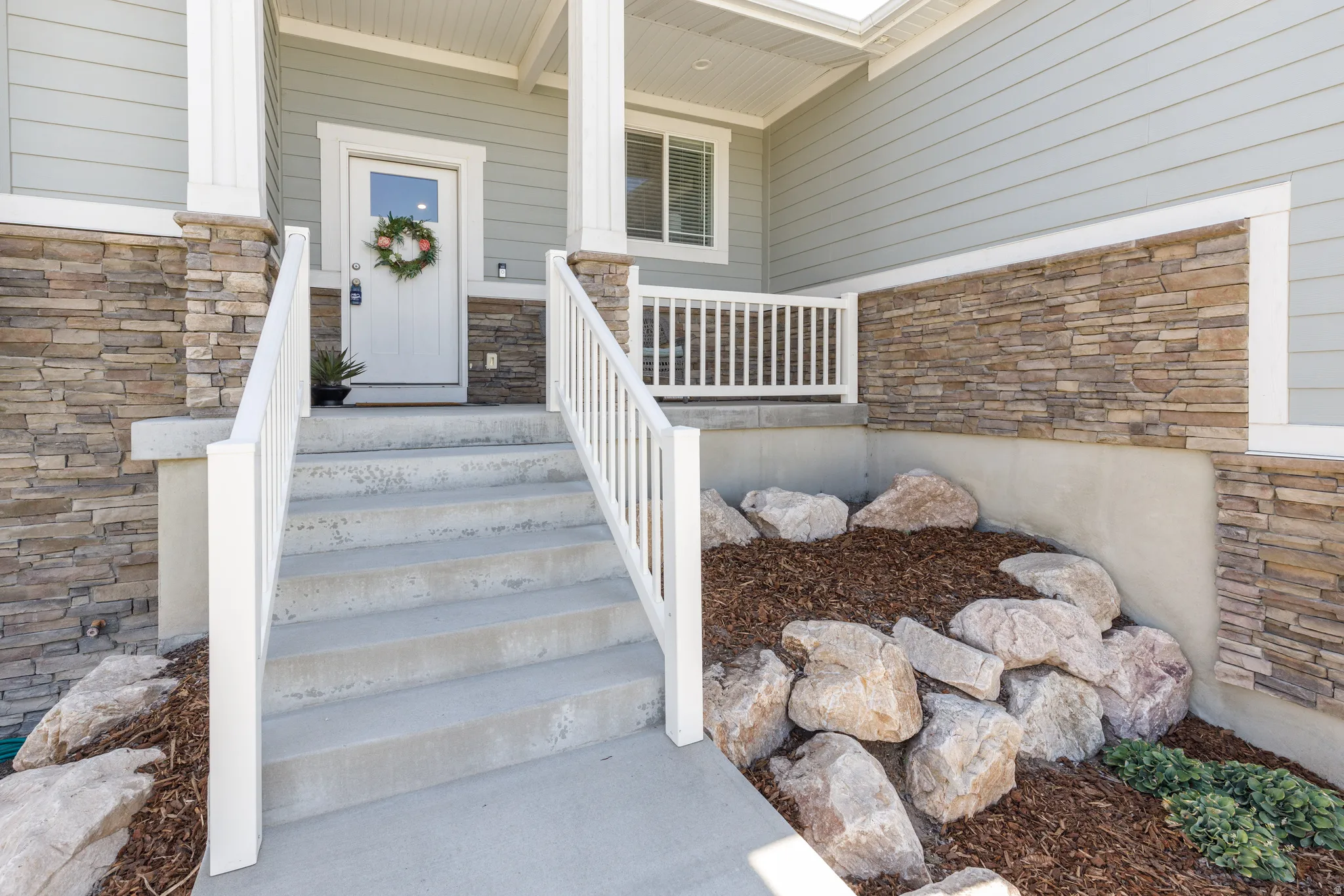 Columned front porch with a white entry door, stone veneer accents, and concrete steps with white railings