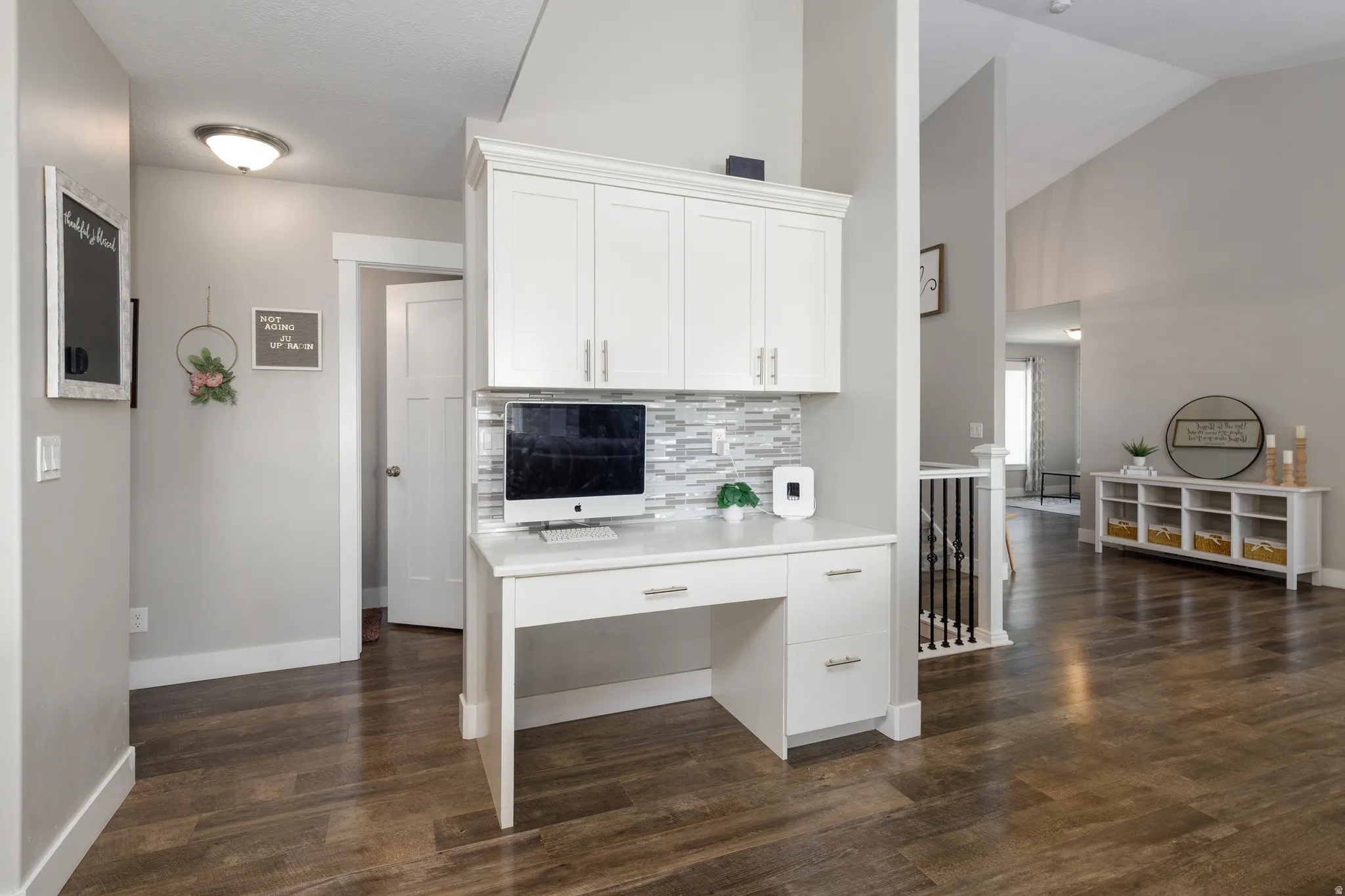 Built-in desk with white cabinetry, tile backsplash, and wood-finish flooring