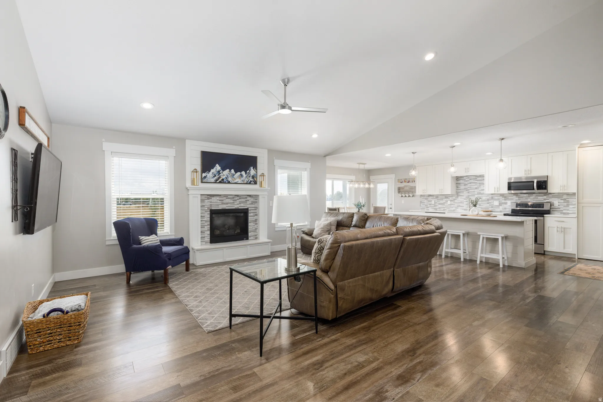 Vaulted ceilings, wood-finish flooring, a stone-surround fireplace, recessed lighting, and a kitchen island with seating