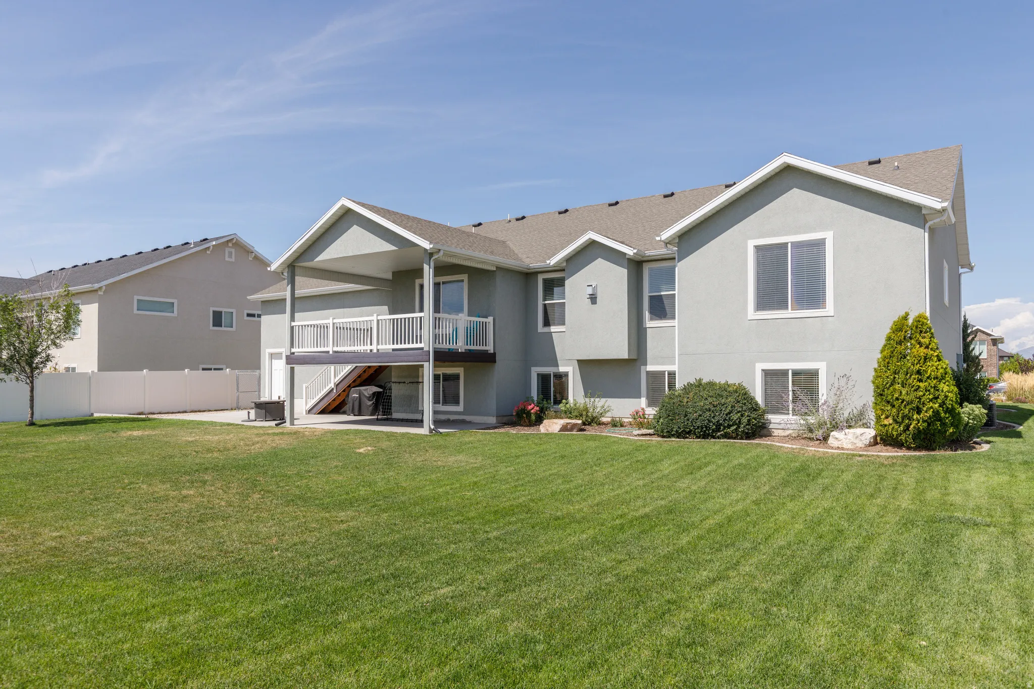 Expansive backyard with a manicured lawn, covered balcony, ground-level patio, and mature landscaping