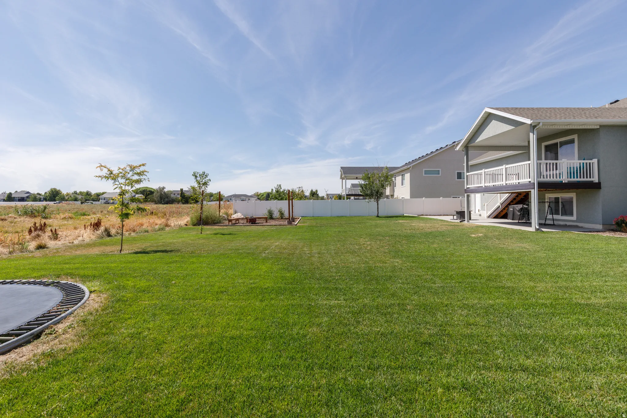 Expansive green lawn, white privacy fencing, multi-level deck, covered patio, and a dedicated outdoor recreation area