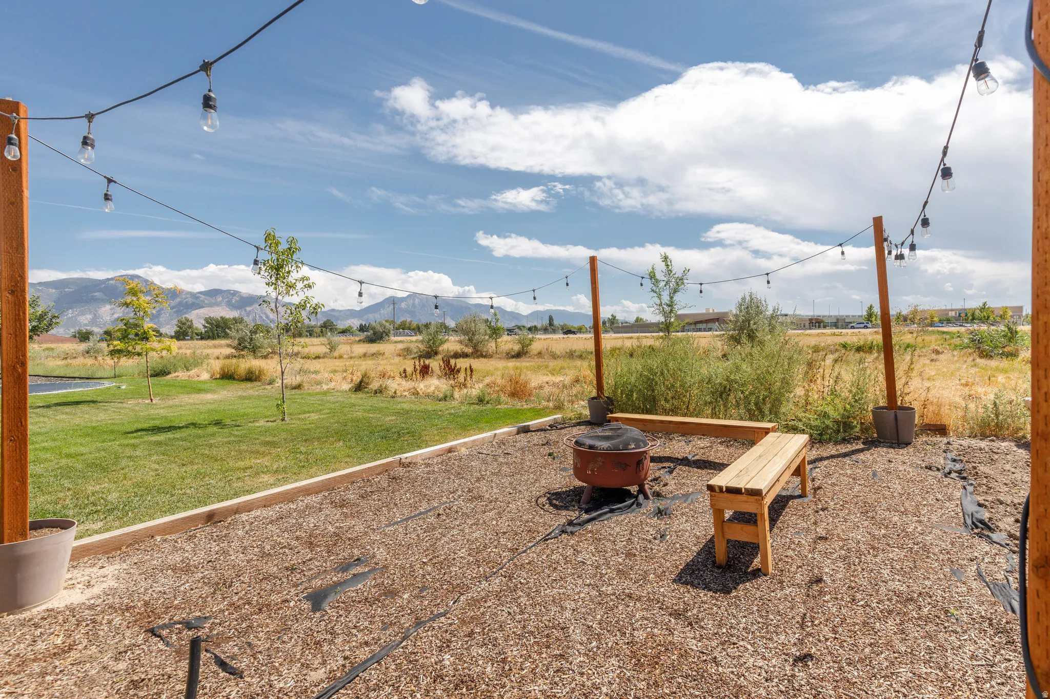 Outdoor entertainment area featuring a gravel patio, string lighting, a fire pit, and built-in benches