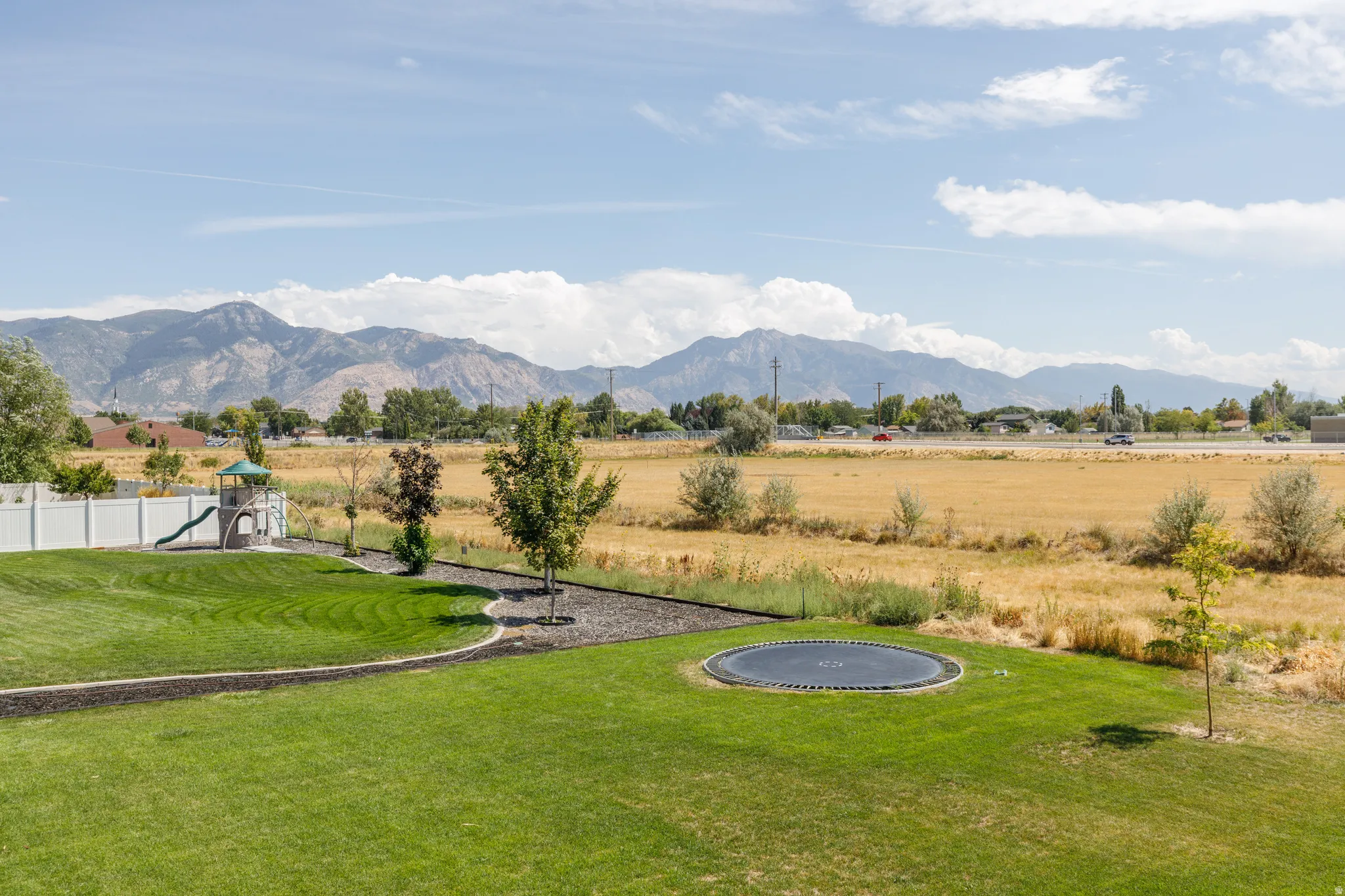 Expansive green lawn with mountain scenery, white privacy fencing, and landscaping