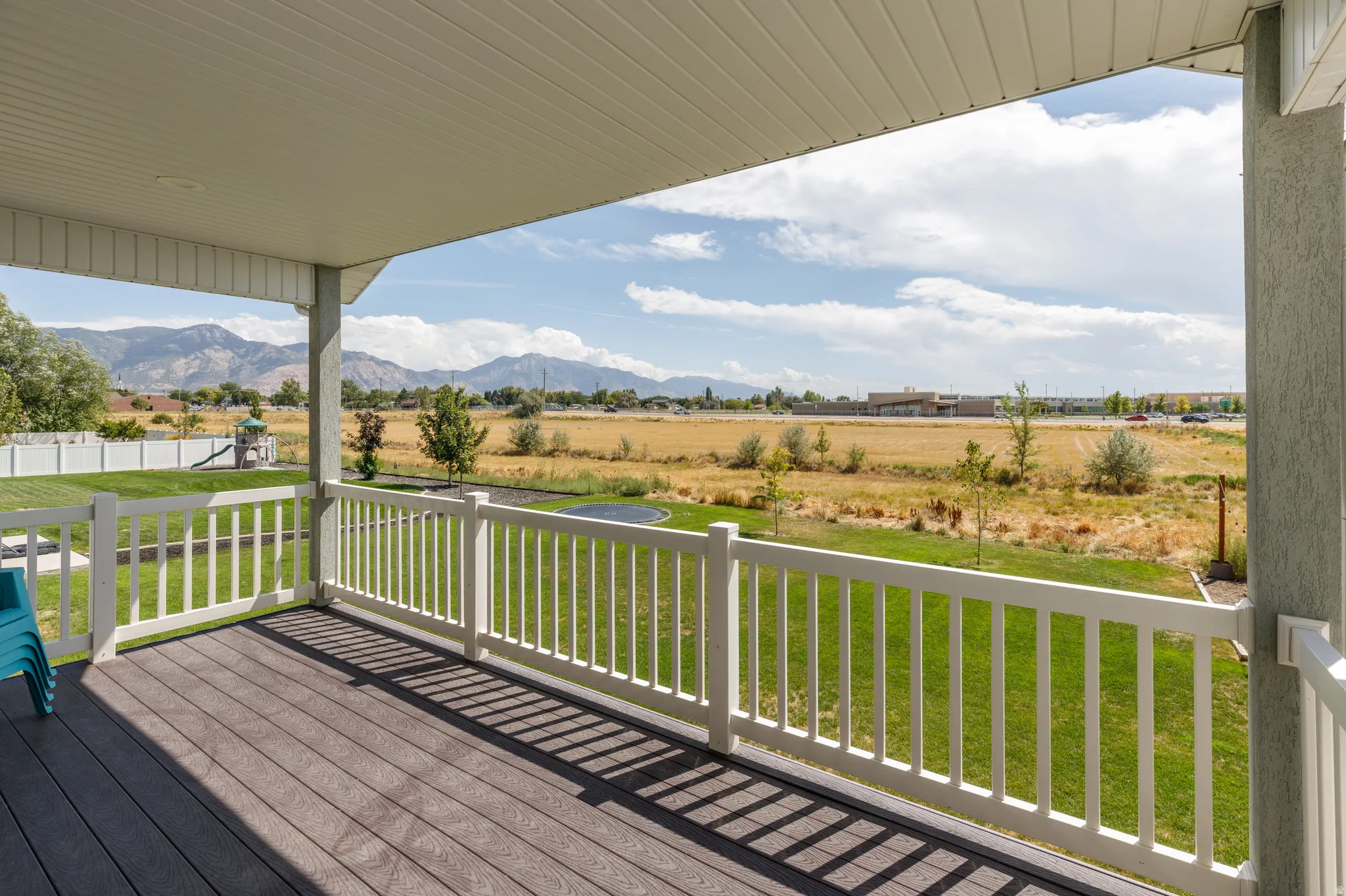 Covered patio featuring wood-finish decking, white railings, and a manicured lawn
