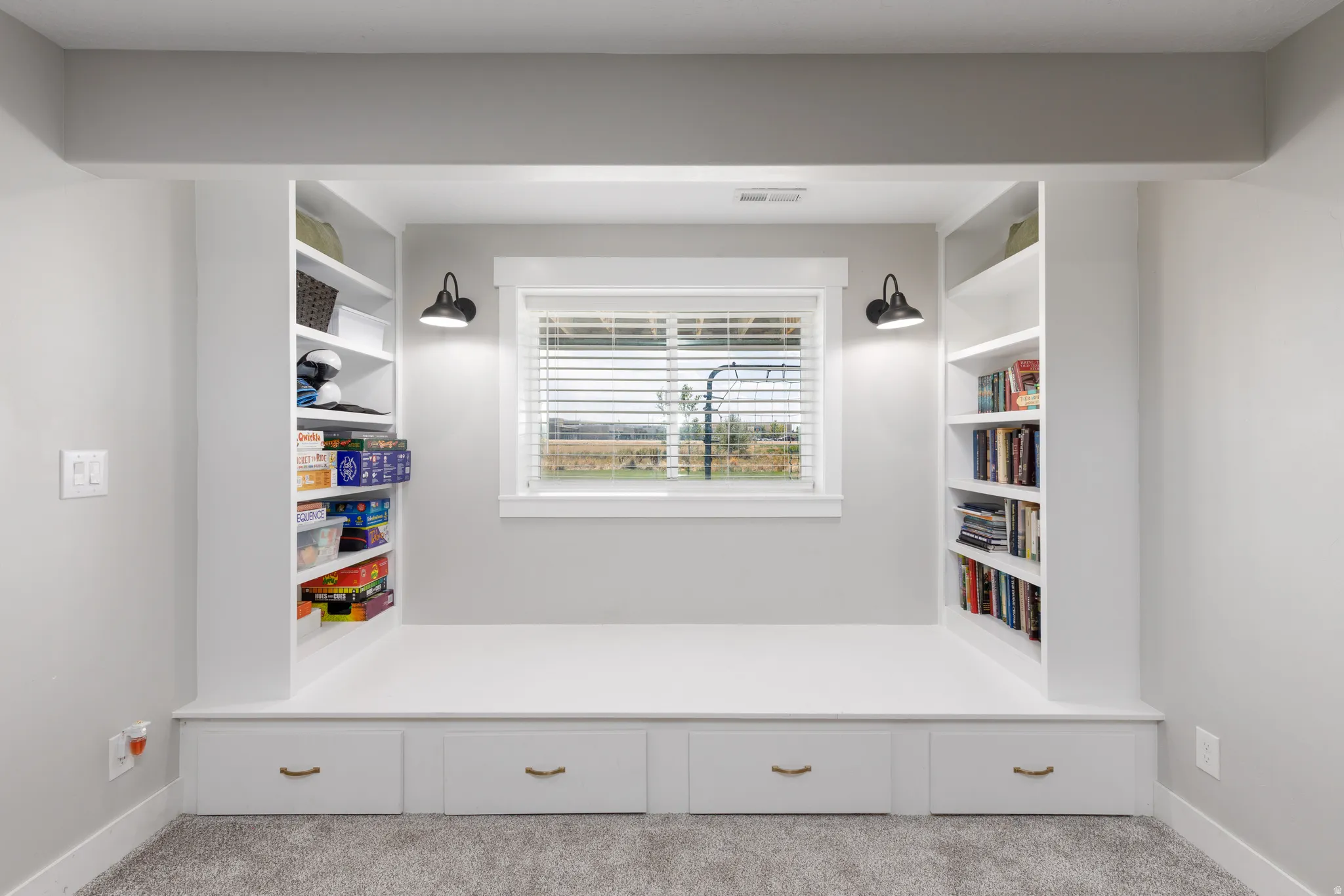 Integrated window seating with built-in storage drawers, flanked by custom shelving, and illuminated by wall-mounted sconces