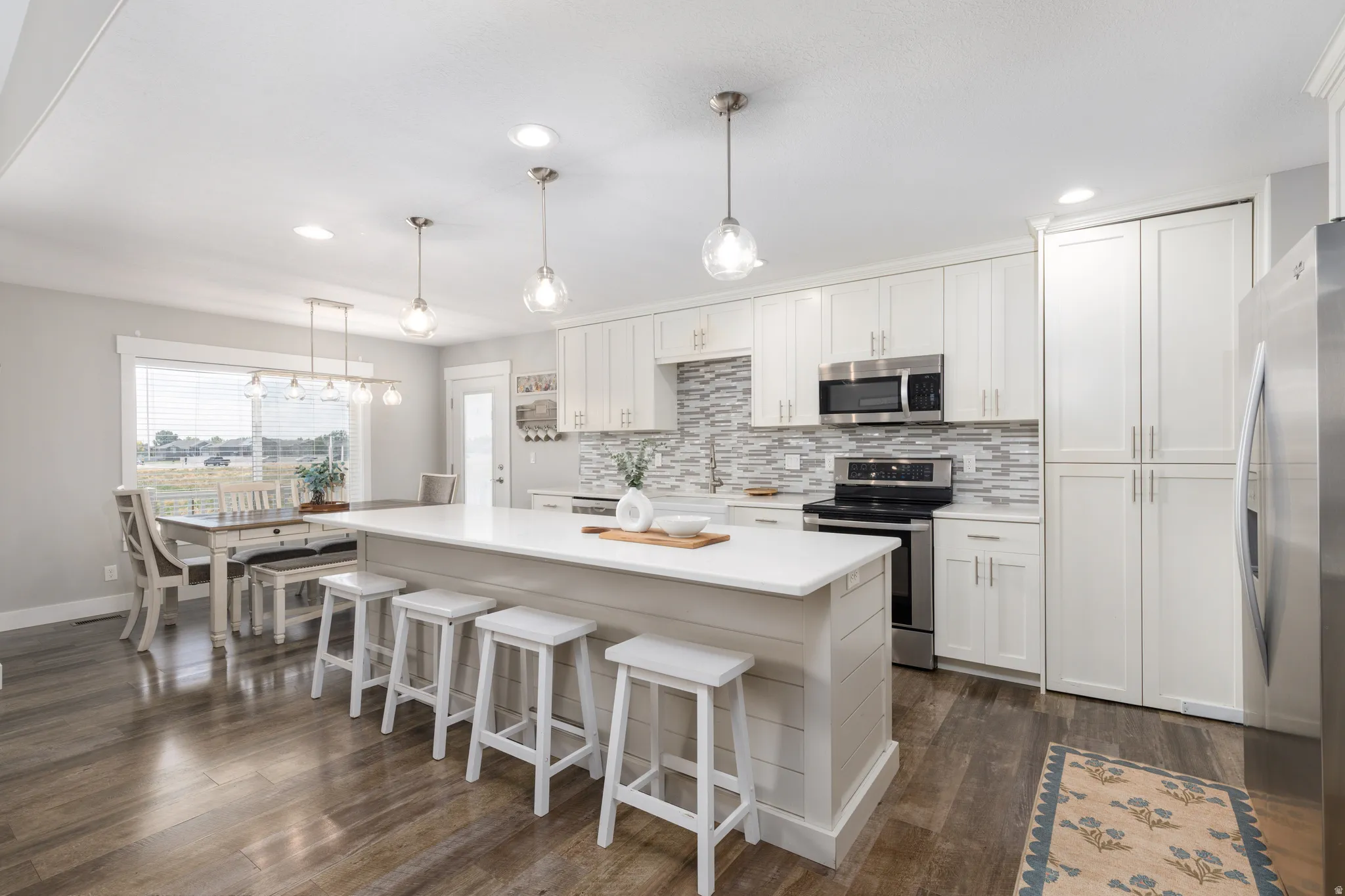 Kitchen featuring white shaker cabinetry, stainless steel appliances, a center island with countertop seating, and wood-finish flooring