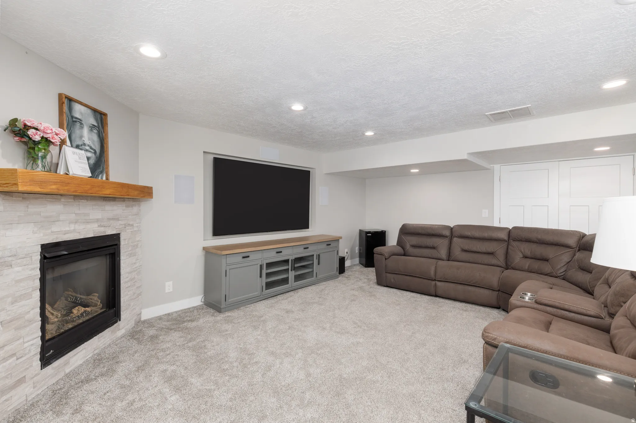 Recessed lighting, stone-clad fireplace with wood mantle, built-in media console, and light gray wall paint