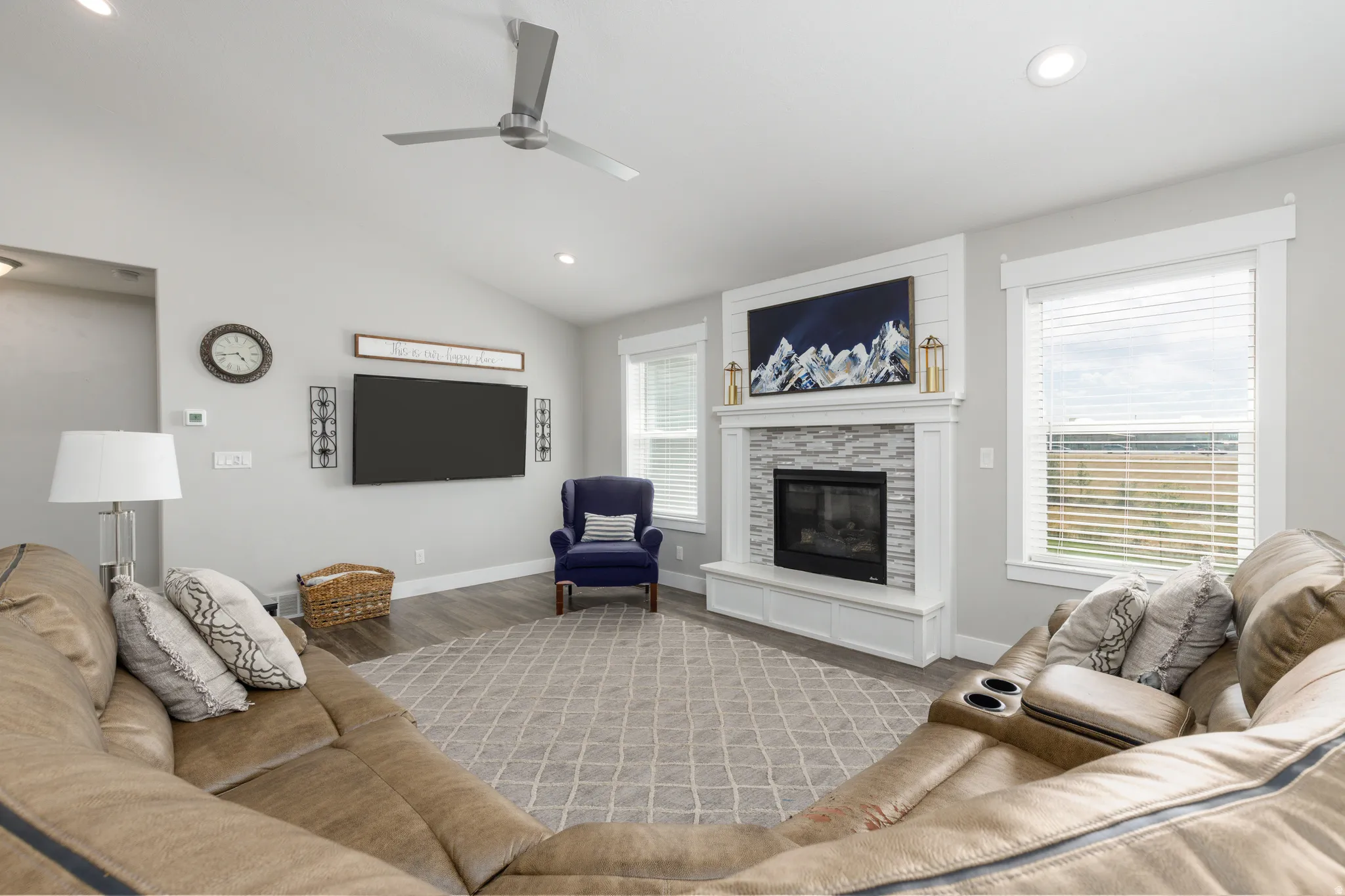 Vaulted ceiling with recessed lighting and ceiling fan, wood-finish flooring, white trim, stone-surround fireplace with mantel, and window blinds