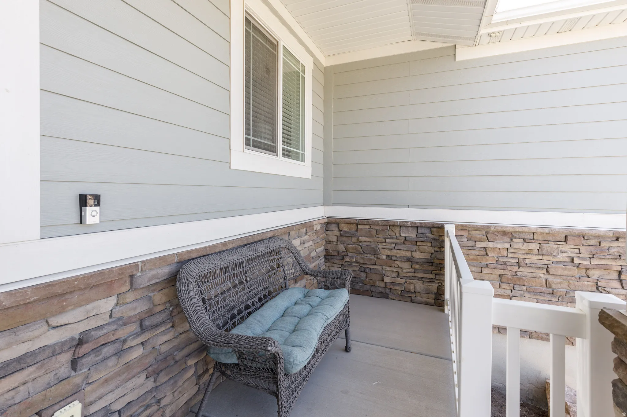 Front porch featuring a stone veneer wainscoting, light gray siding, white window trim, and a white railing