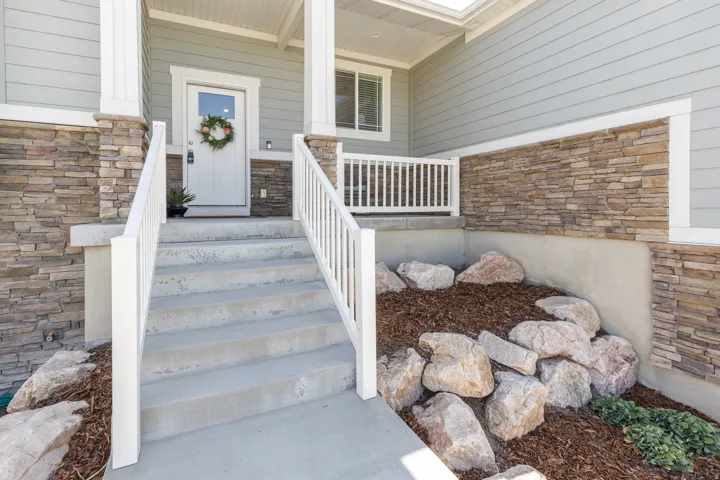Columned front porch with a white entry door, stone veneer accents, and concrete steps with white railings