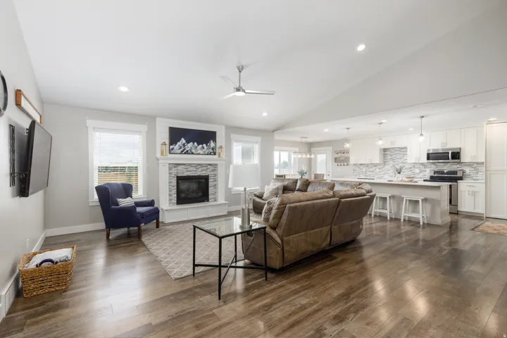 Vaulted ceilings, wood-finish flooring, a stone-surround fireplace, recessed lighting, and a kitchen island with seating