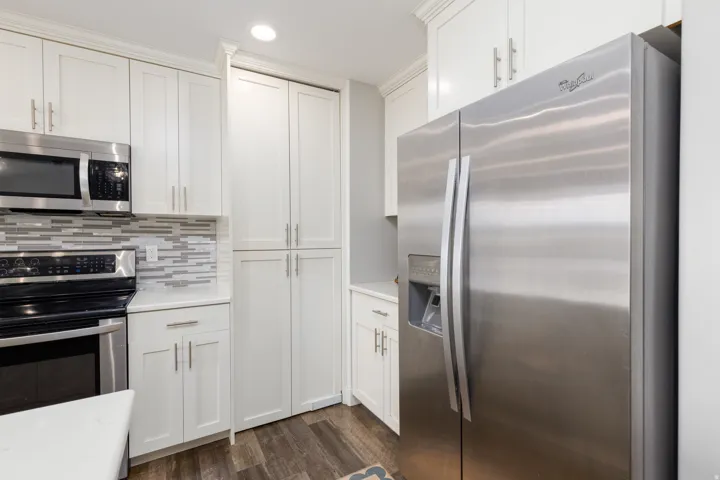 White shaker-style cabinetry with crown molding, stainless steel appliances, a mosaic tile backsplash, wood-finish flooring, and solid surface countertops