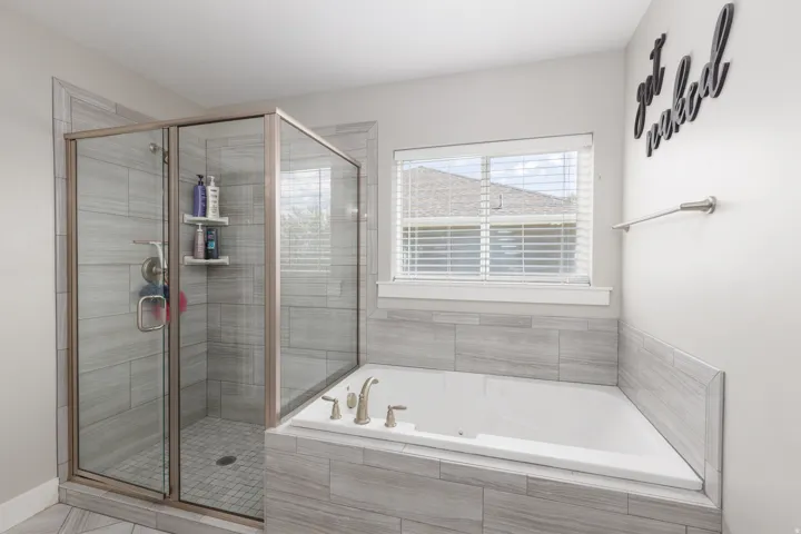 Glass-enclosed shower with tile surround, built-in soaking tub, and tile-wrapped tub deck