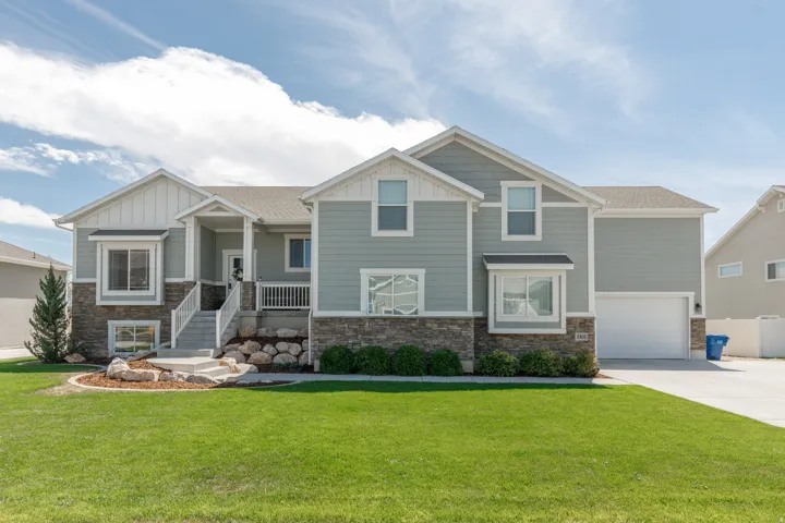 Exterior features a stone and siding facade, covered front porch, integrated two-car garage, and a manicured front lawn