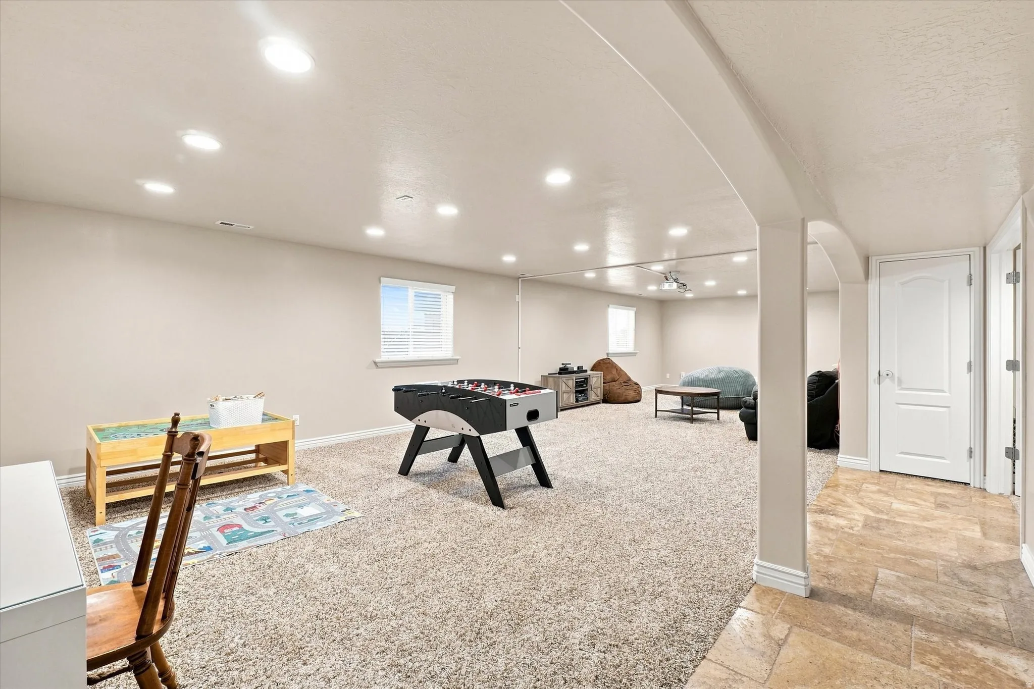 Recessed lighting throughout, two windows, wall-to-wall carpeting, arched structural elements, and a white paneled door with a contrasting handle