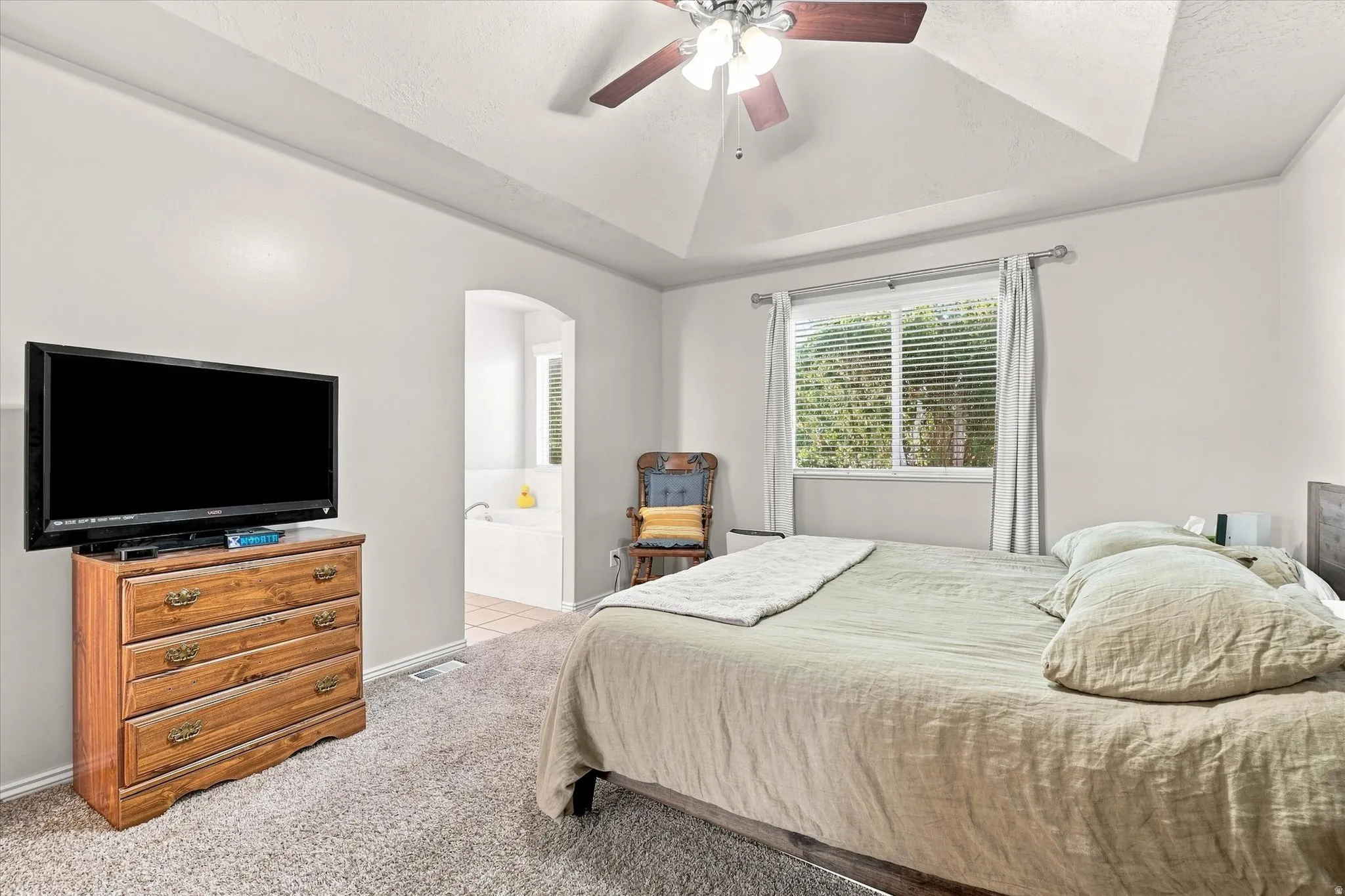 Vaulted ceiling with ceiling fan, carpet flooring, window with blinds, and an arched doorway leading to a built-in tub