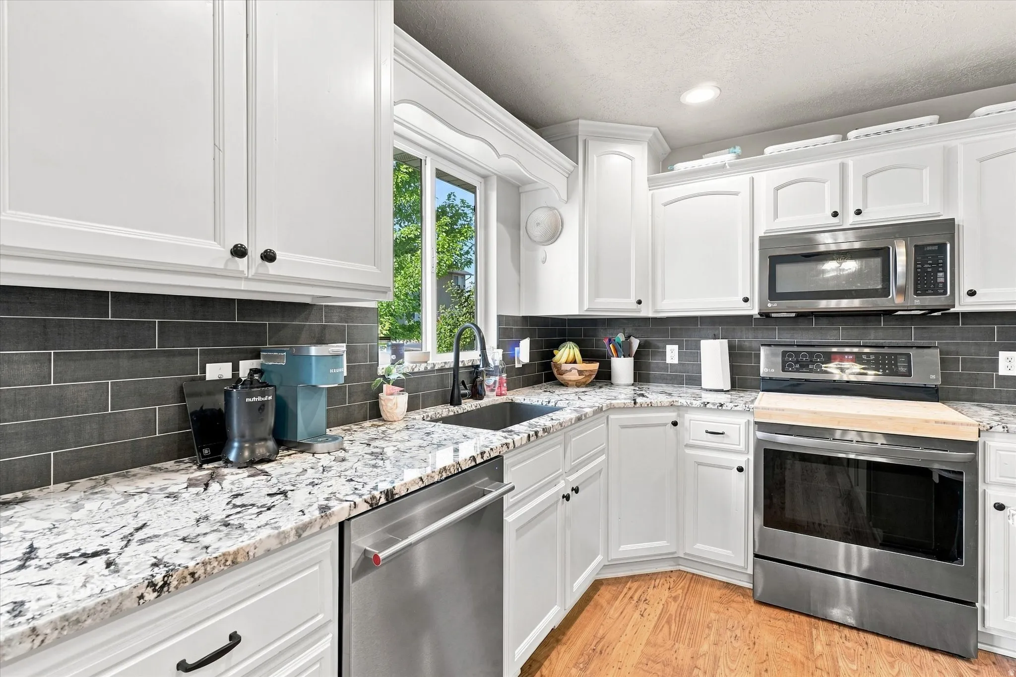 White cabinetry with dark hardware, granite countertops, subway tile backsplash, stainless steel appliances, and wood-finish flooring