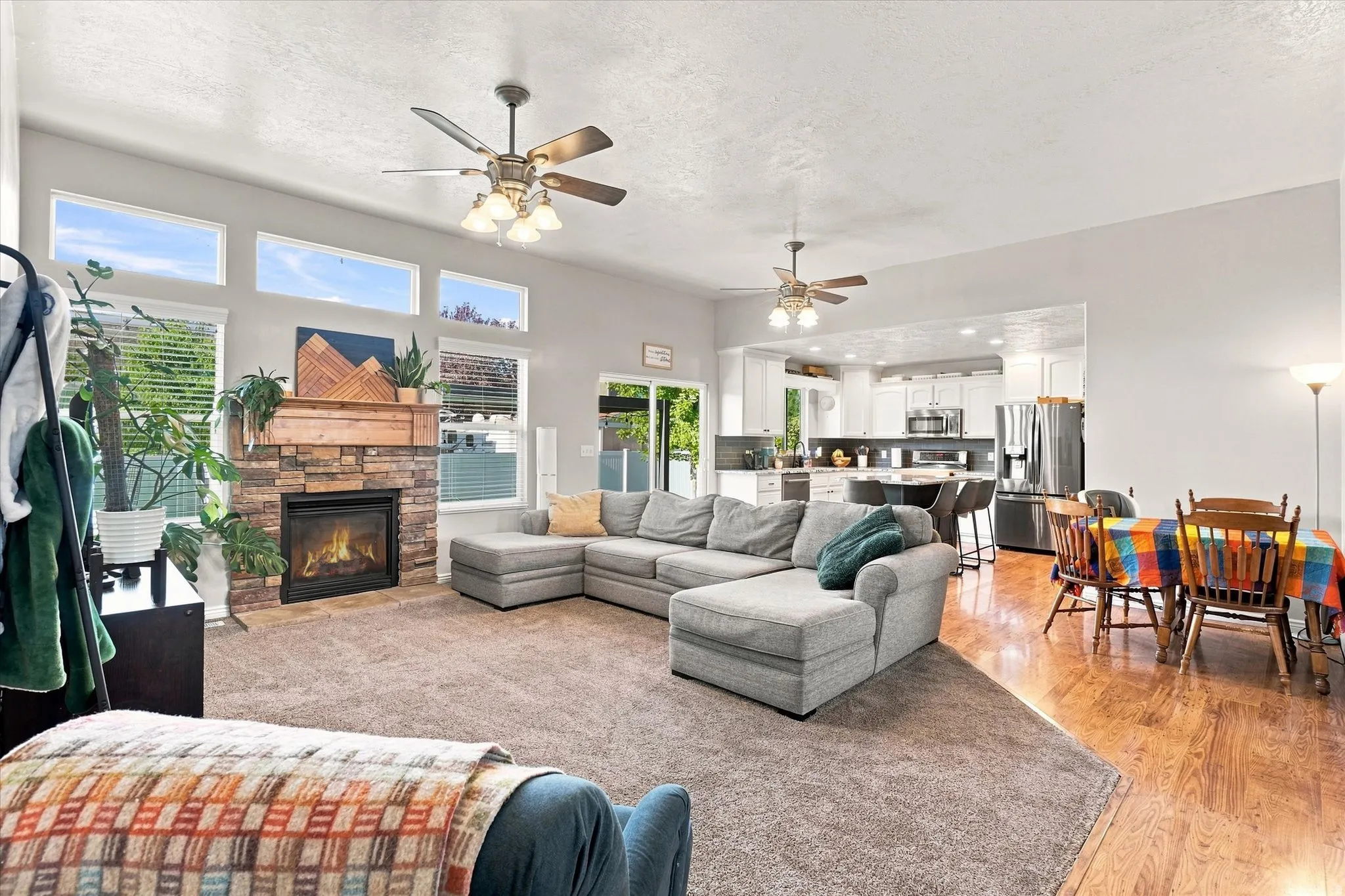 Open-concept living area featuring a stone-clad fireplace, wood mantel, and multiple transom windows