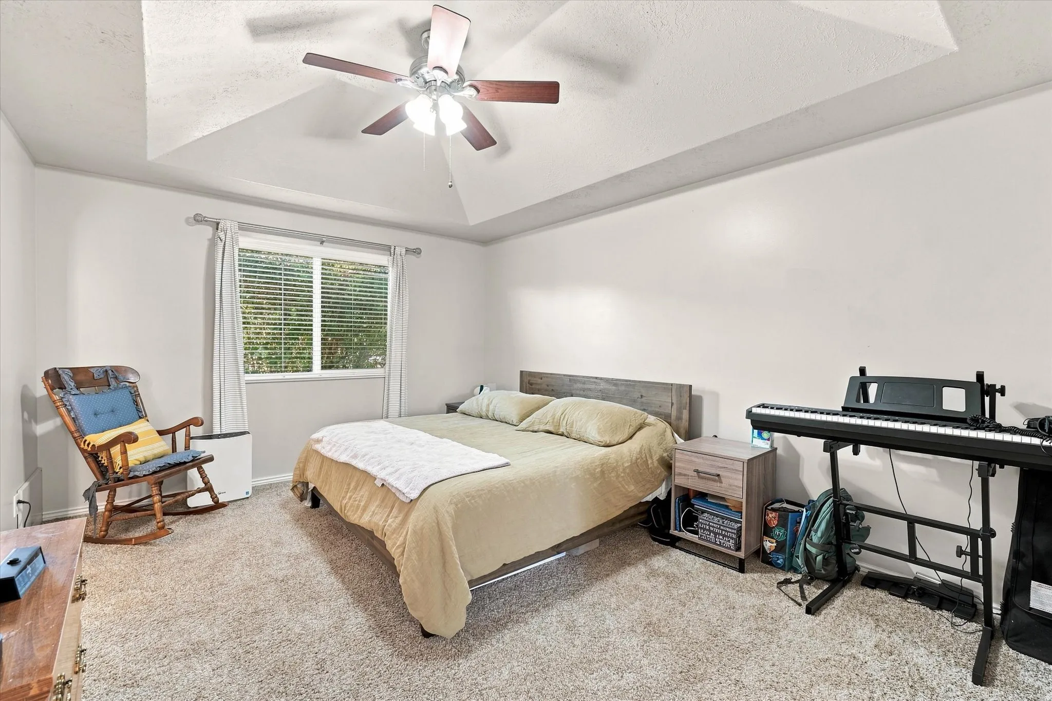 Tray ceiling with a ceiling fan, light-colored carpet, and a window with blinds