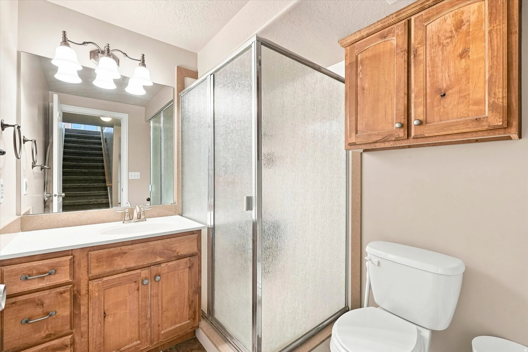 Wood-finish vanity with a white countertop and undermount sink, complemented by a three-light fixture