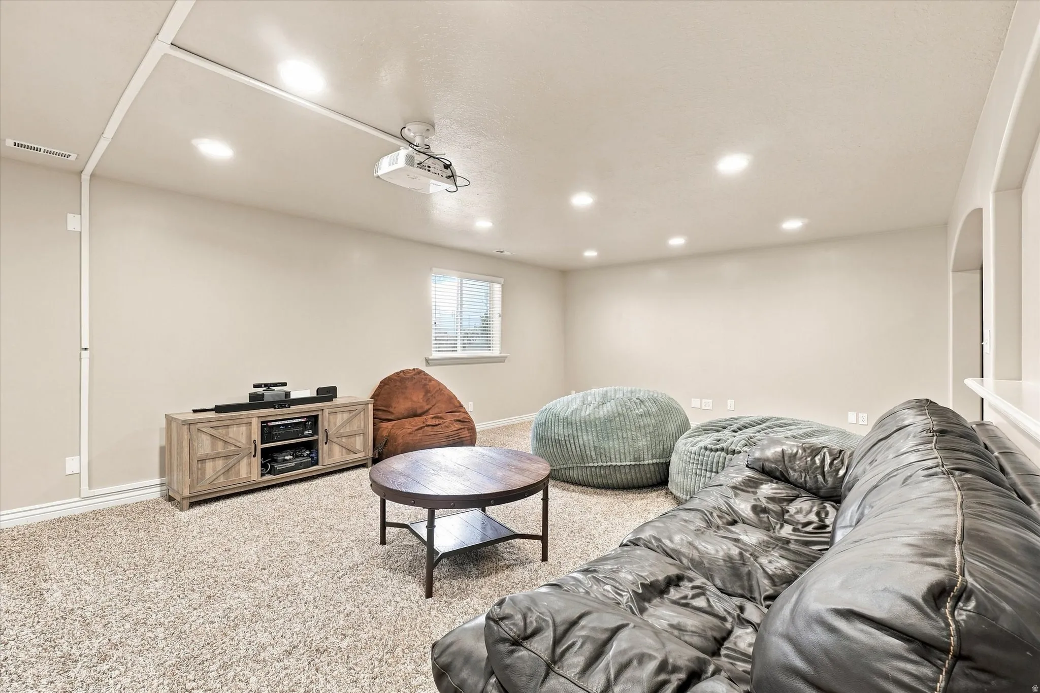 Recessed ceiling lighting, ceiling-mounted projector, wall-mounted projection screen, single window with blinds, light-toned carpeting