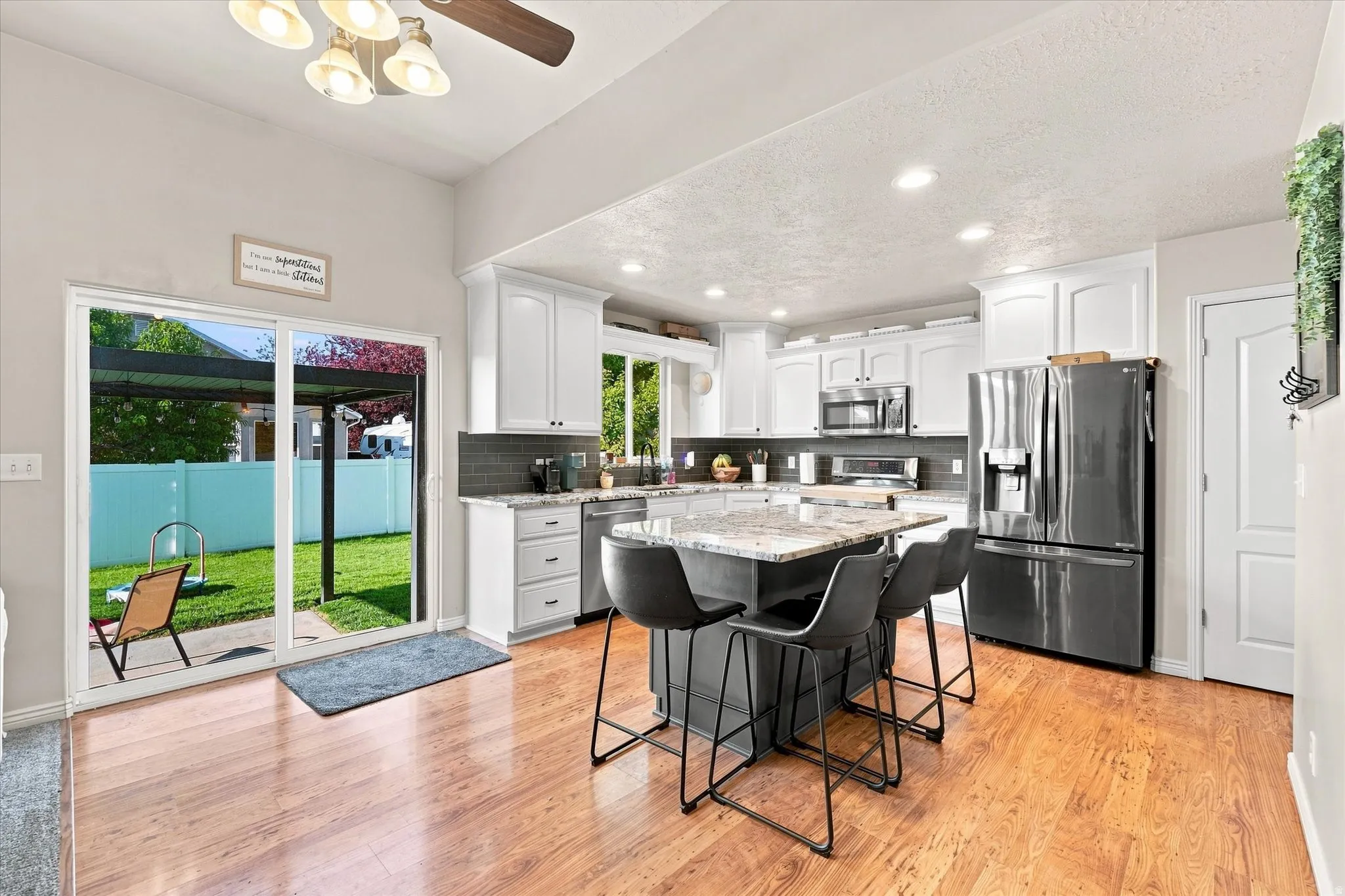 Modern kitchen featuring wood-finish flooring, white cabinetry, recessed lighting, a center island with a stone countertop, and stainless steel appliances