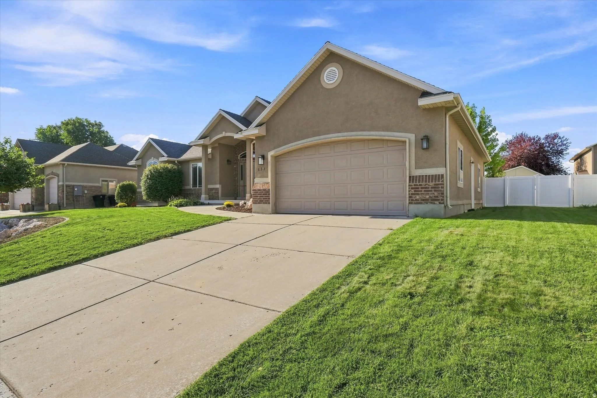 Stucco exterior with brick detailing, an arched garage door, concrete driveway, and a white privacy fence