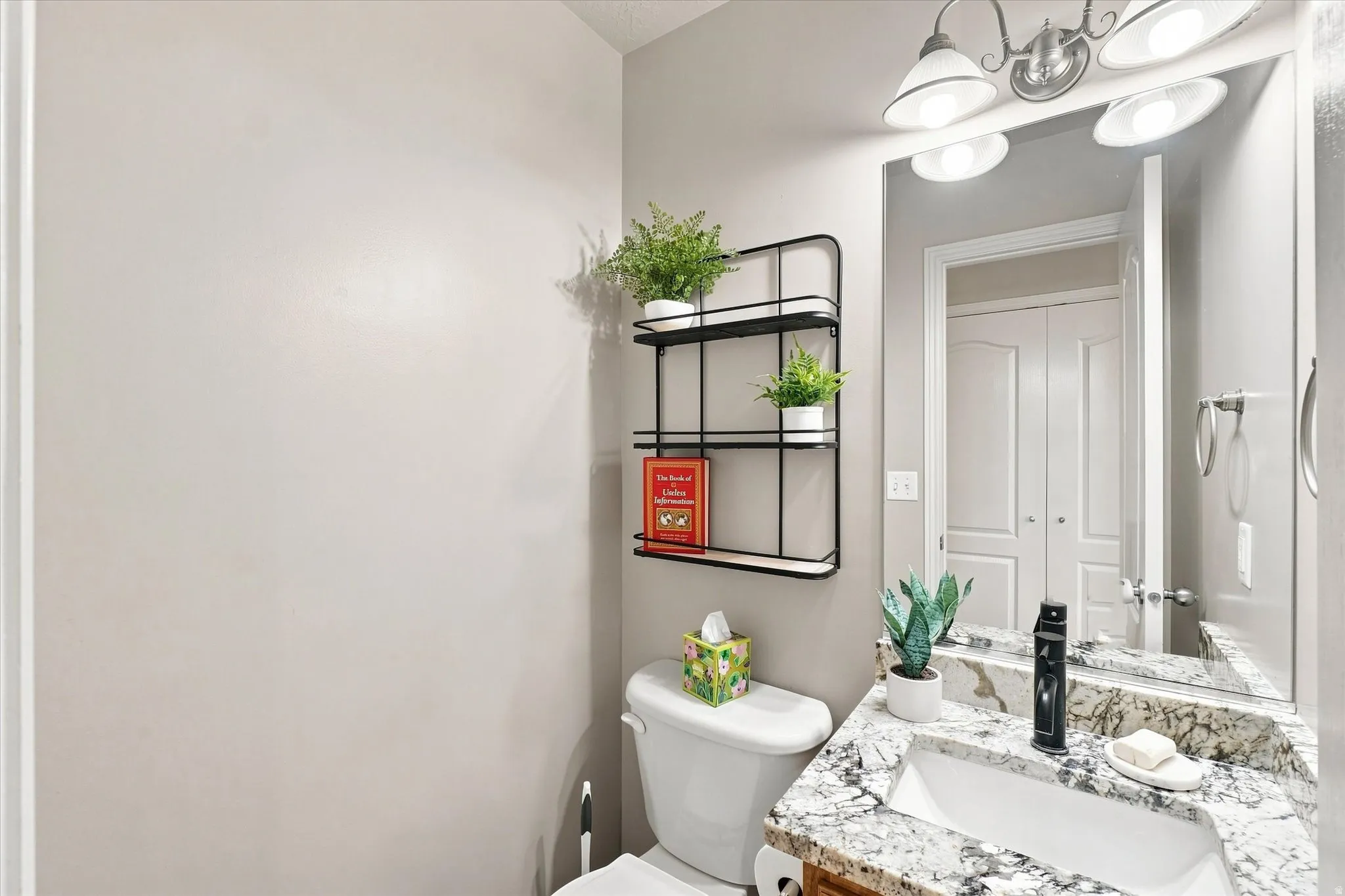Bathroom featuring a vanity with a stone countertop, an integrated sink, a wall-mounted mirror, and a wall-mounted light fixture