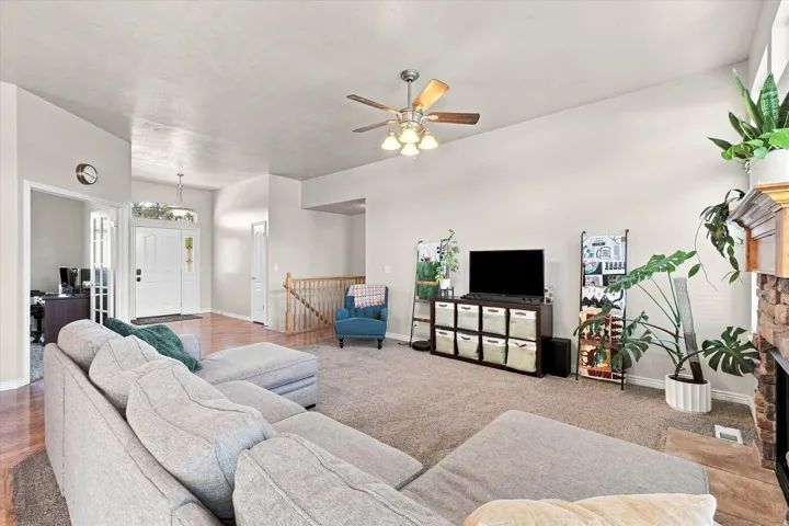 Carpeted living area with a ceiling fan light fixture, stone-clad fireplace, and wood-finish flooring