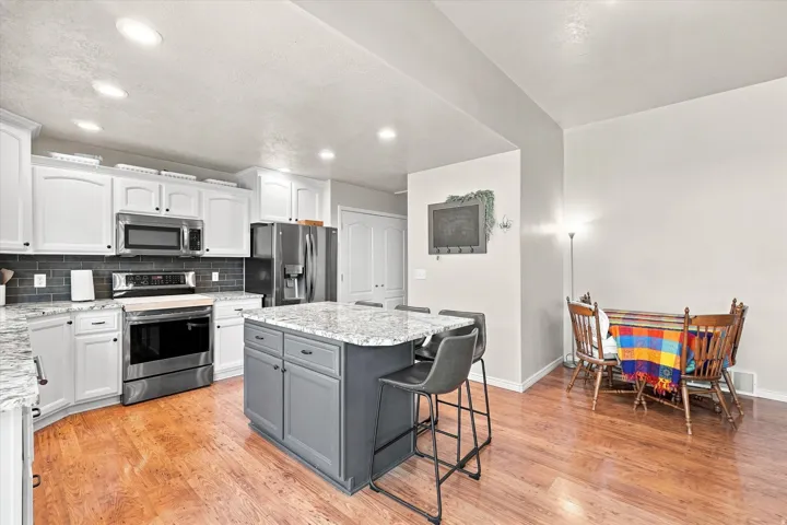 Kitchen featuring white cabinetry, stainless steel appliances, a dark tile backsplash, and an island with a light-toned countertop