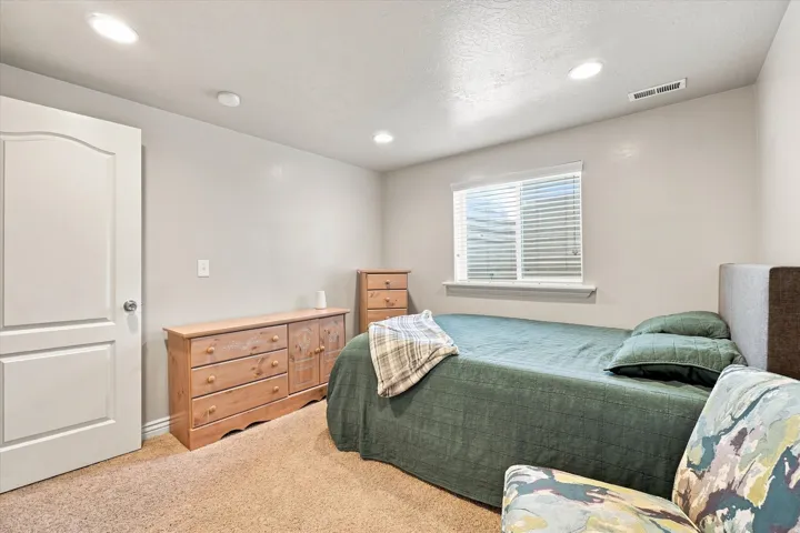 Recessed lighting illuminates the room, featuring a window with horizontal blinds and neutral-toned carpeting
