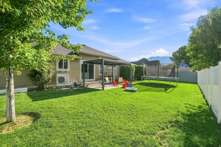 Expansive backyard featuring a manicured lawn, a white privacy fence, and a patio with an attached pergola