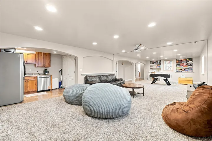 Expansive carpeted room featuring a built-in wet bar with wood cabinetry, a stainless steel refrigerator, and a stainless steel dishwasher