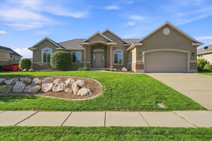 Stucco exterior with brick accents, arched entry, arched windows, attached garage, and landscaped rock garden