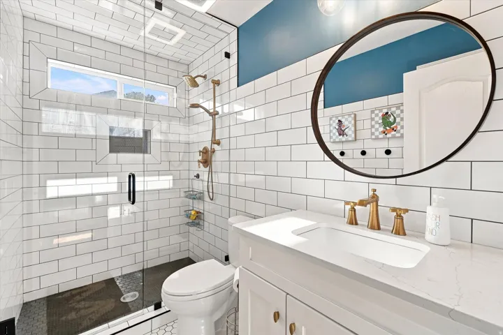 Glass-enclosed shower with subway tile surround, transom window, and a dark tile shower flooring