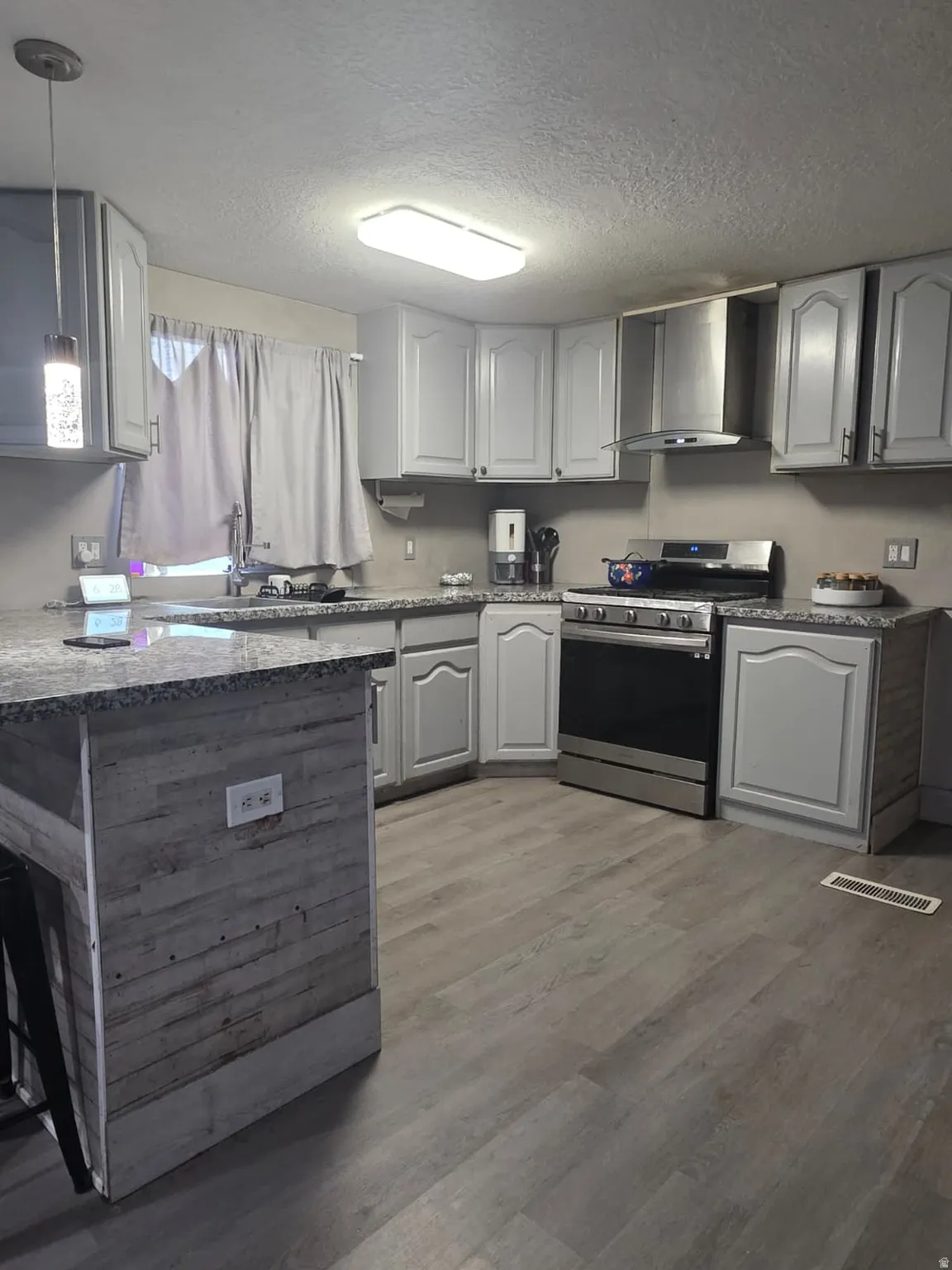 Kitchen featuring light gray cabinetry, stainless steel appliances, granite-style countertops, wood-finish flooring, and a breakfast bar