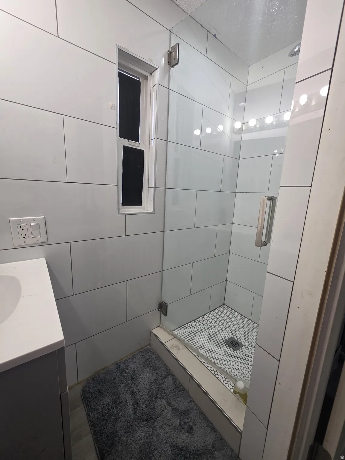 Floor-to-ceiling white tile, walk-in shower with clear glass enclosure, penny tile shower floor, and a rectangular window