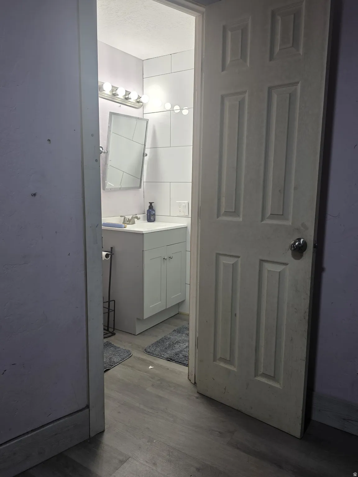 White subway tile backsplash, vanity with under-sink cabinetry, chrome faucet, and wood-finish flooring