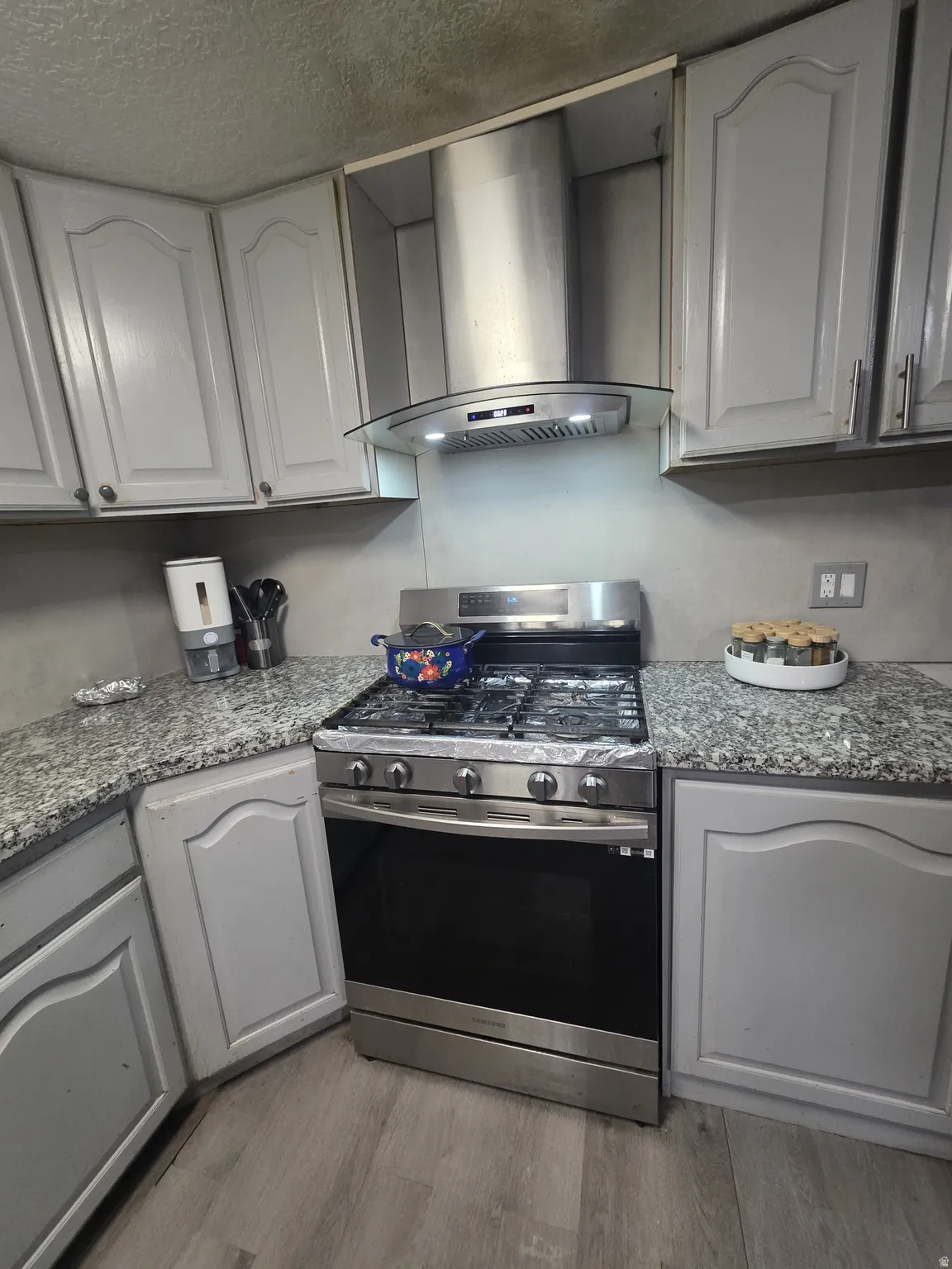 Stainless steel range with a coordinating hood, light gray cabinetry, and stone-finish countertops