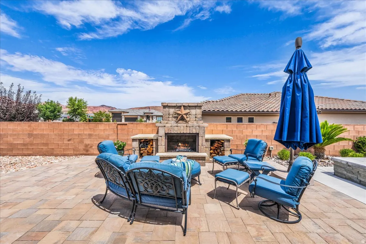 Paver patio featuring a stone fireplace, built-in firewood storage, and a low-maintenance landscape design