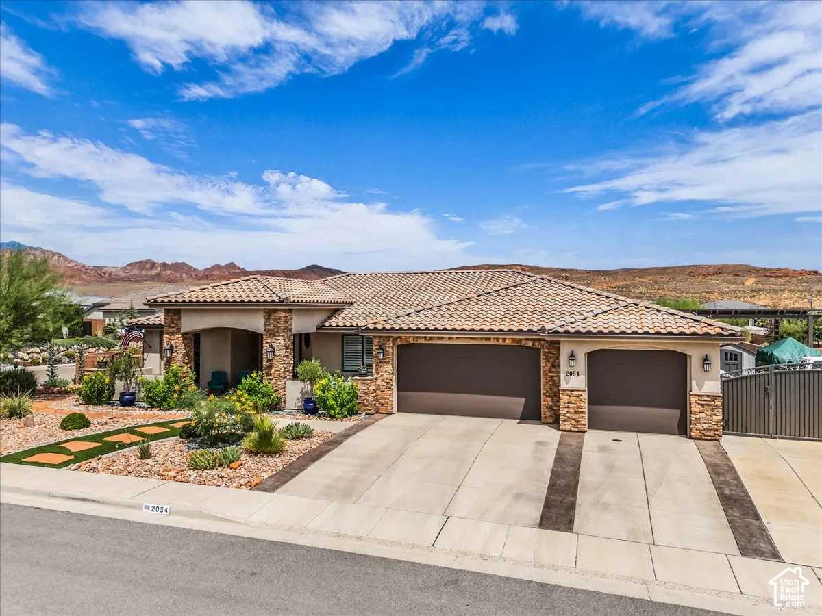 Mediterranean-style exterior with a tile roof, stone accents, two-car garage, and desert landscaping