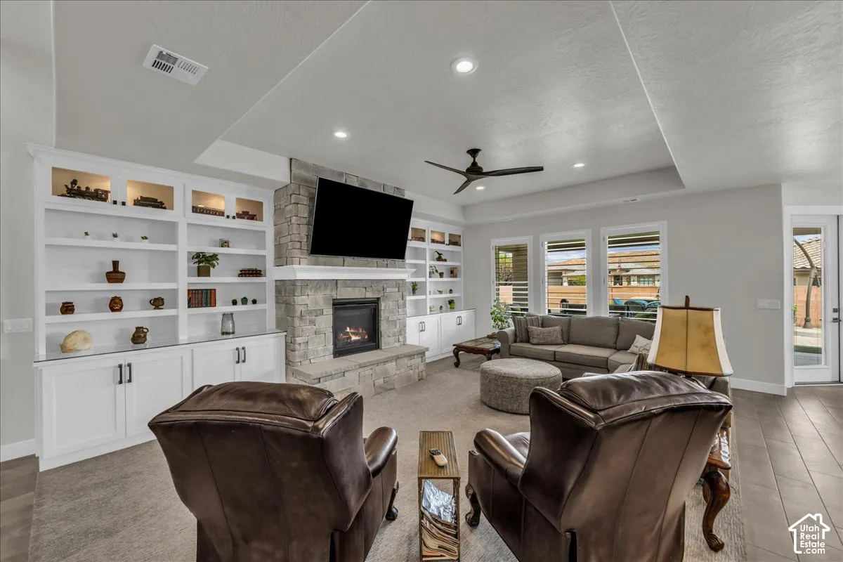 Stone surround fireplace with built-in cabinetry, tray ceiling, recessed lighting, and wood-finish flooring