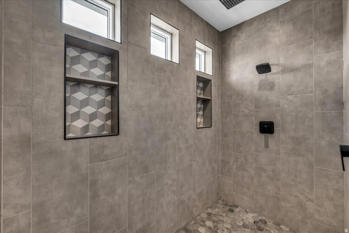 Spa-inspired shower featuring large-format gray tile walls, recessed shelving with geometric tile accent, skylight windows for natural illumination, and dual wall-mounted fixtures