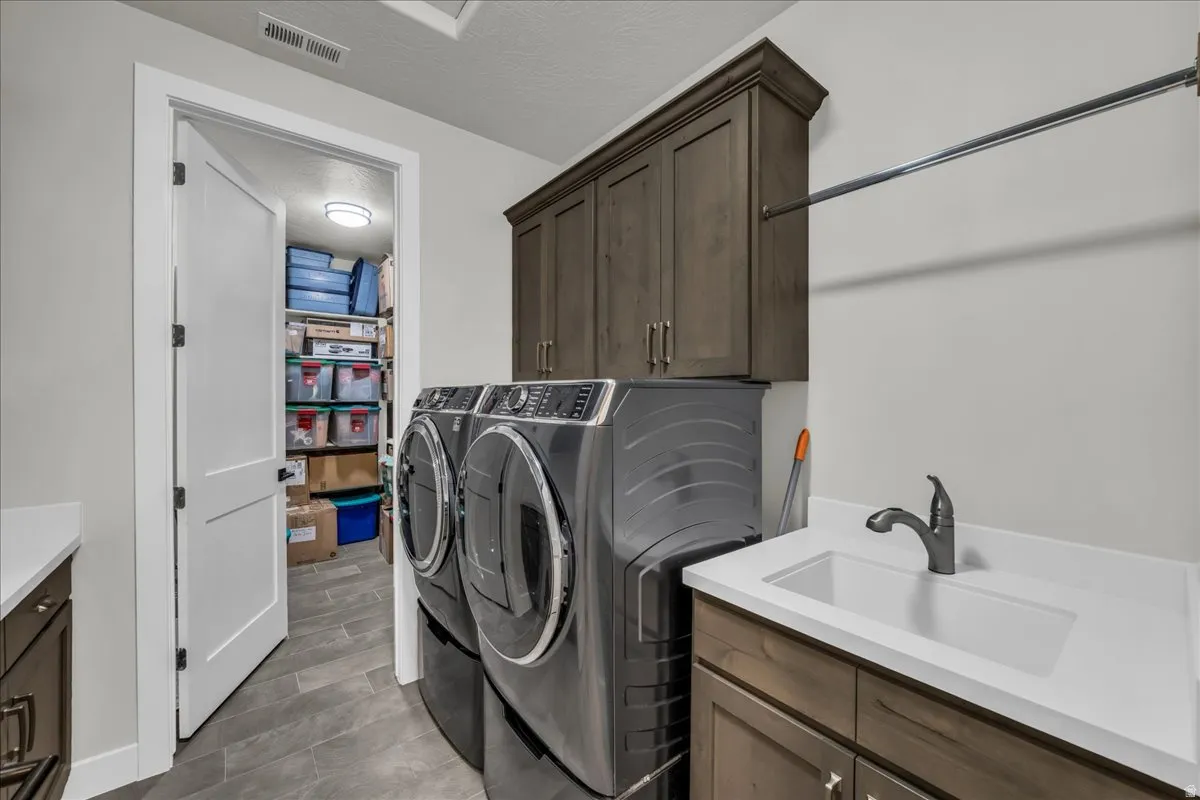 Laundry room featuring wood-finish cabinetry, solid surface countertop with integrated sink, and a hanging rod