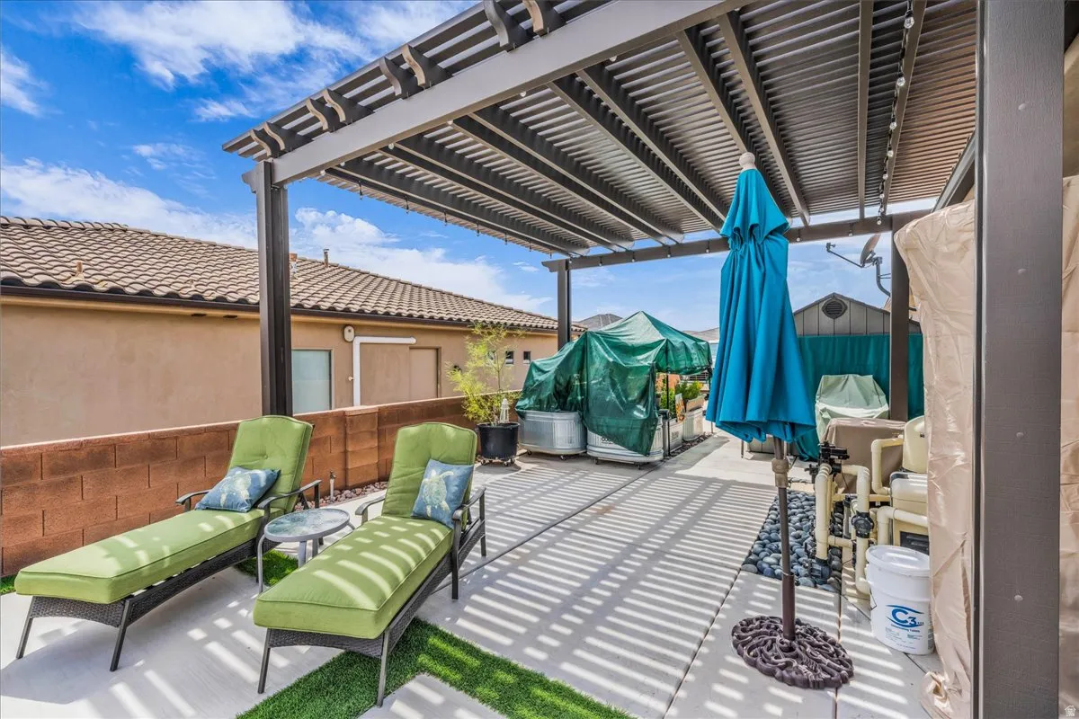 Patio featuring a slatted pergola, concrete flooring, artificial turf accents, and a block privacy wall