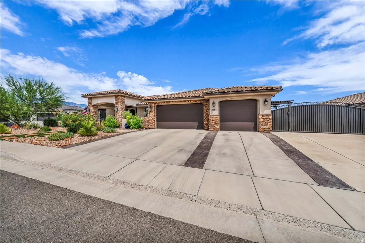 Stucco exterior featuring stone accents, a tile roof, an integrated two-car garage, and a large concrete driveway with decorative banding