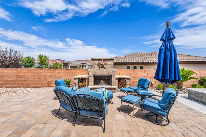 Paver patio featuring a stone fireplace, built-in firewood storage, and a low-maintenance landscape design